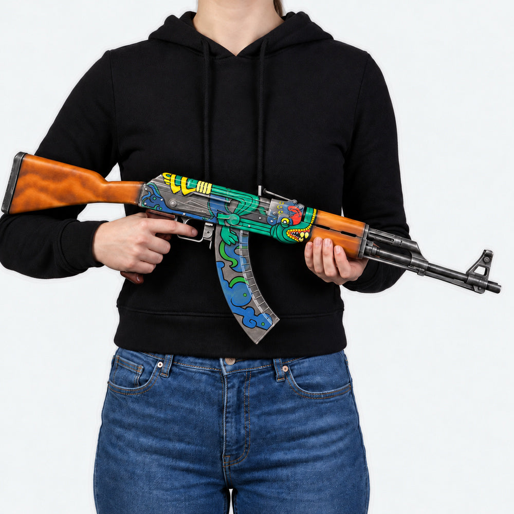Woman in a black hoodie and blue jeans holding the AK-47 Fire Serpent prop across her body, with the muzzle pointing to the right.