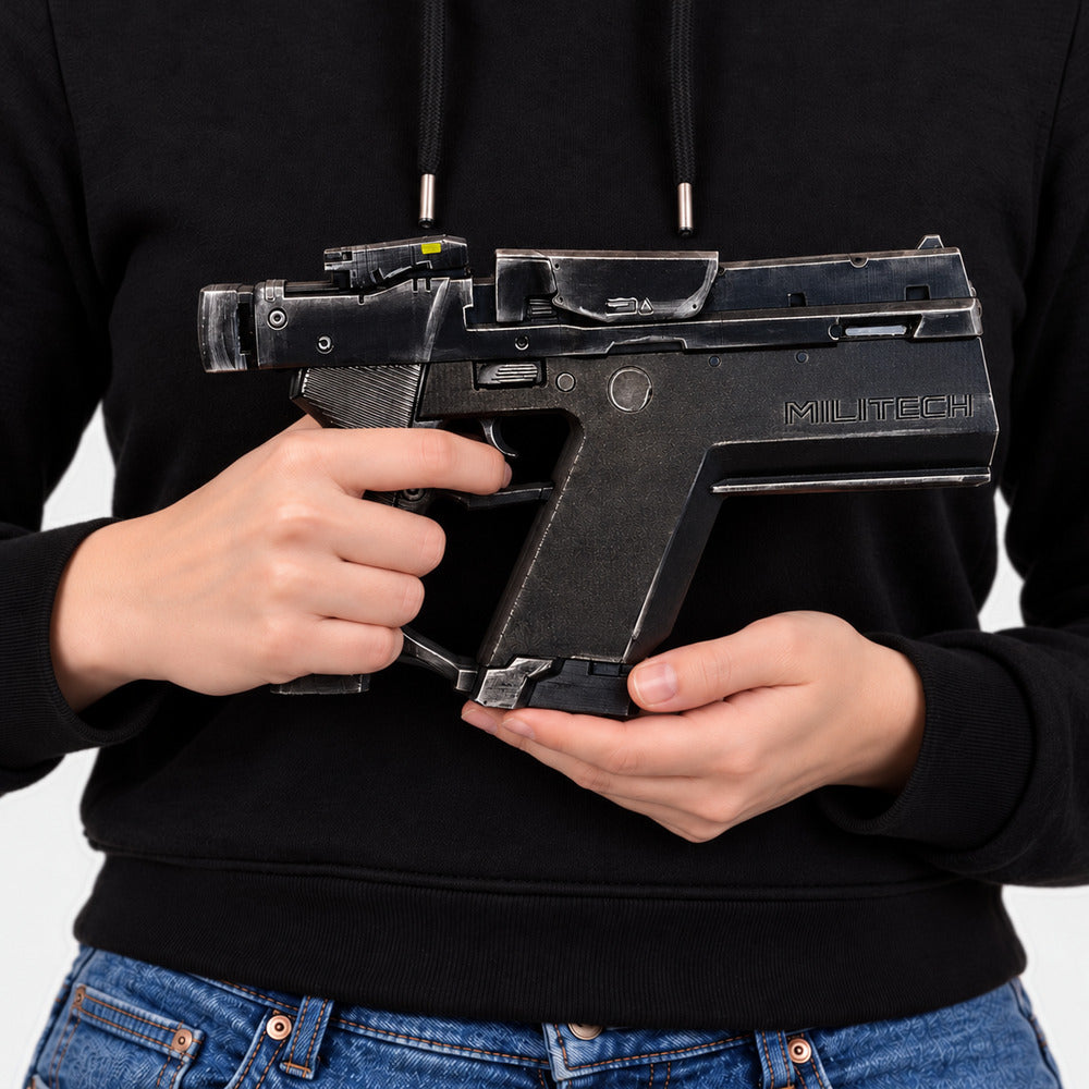 Woman in a black hoodie and jeans holding the black-and-silver Cyberpunk Pariah pistol prop across her body, with its MILITECH side visible and muzzle pointing right.
