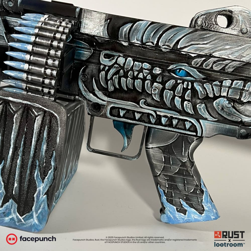 Close-up of the Frost M249 receiver: a painted dragon head with a blue eye and long white teeth, ammo belt above.